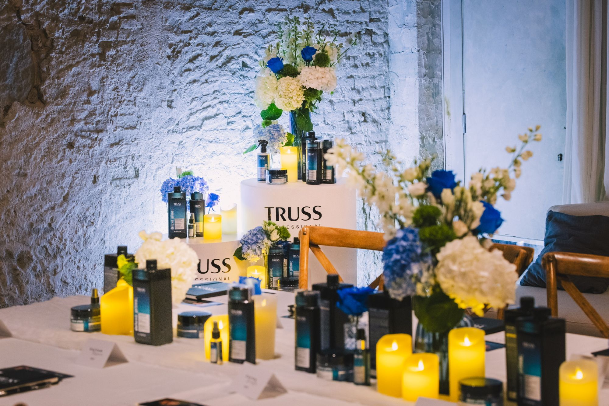 The dressed room: a lit product plinth against whitewashed stone, with florals and candles along the table